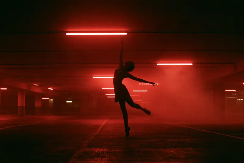 Graded in Red — a dancer in silhouette mid-turn in an empty car park, the whole frame graded deep red under strip lights