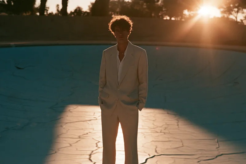Low Sun — a figure in a cream suit standing in an empty swimming pool, backlit by a low sun