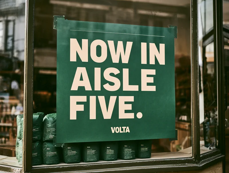 Volta Coffee — a green poster in a grocery window reading Now in aisle five.
